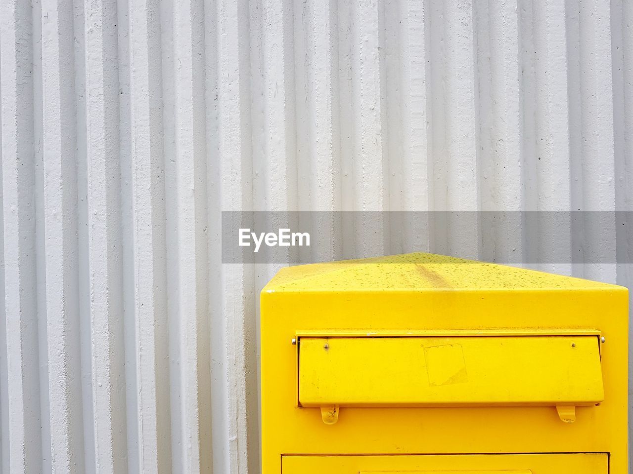 Yellow mailbox against corrugated iron