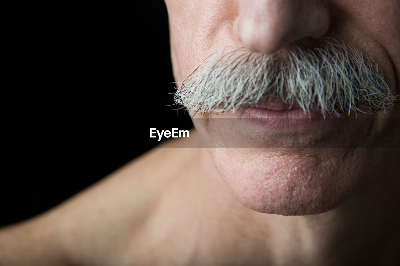 Midsection of man with mustache against black background