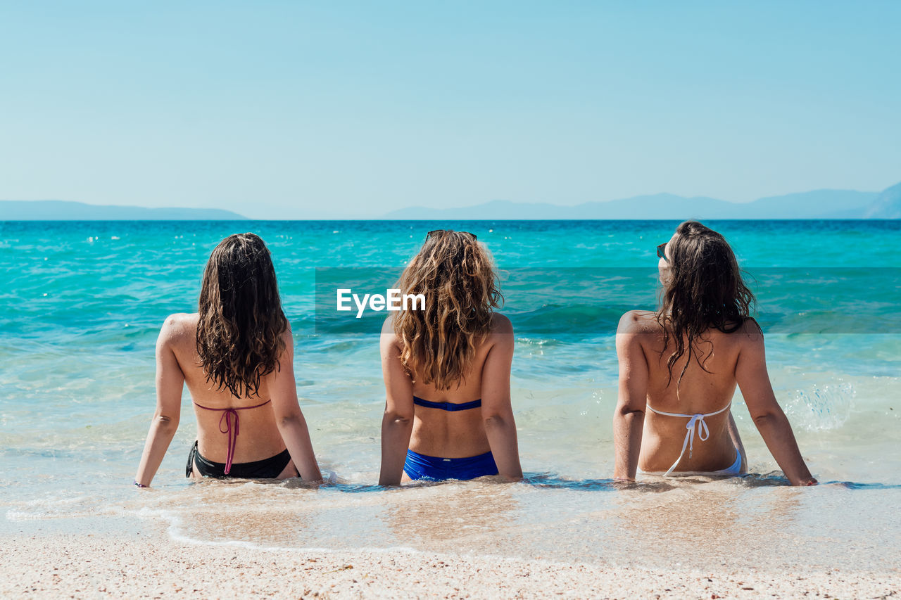 Rear view of female friends sitting on shore at beach