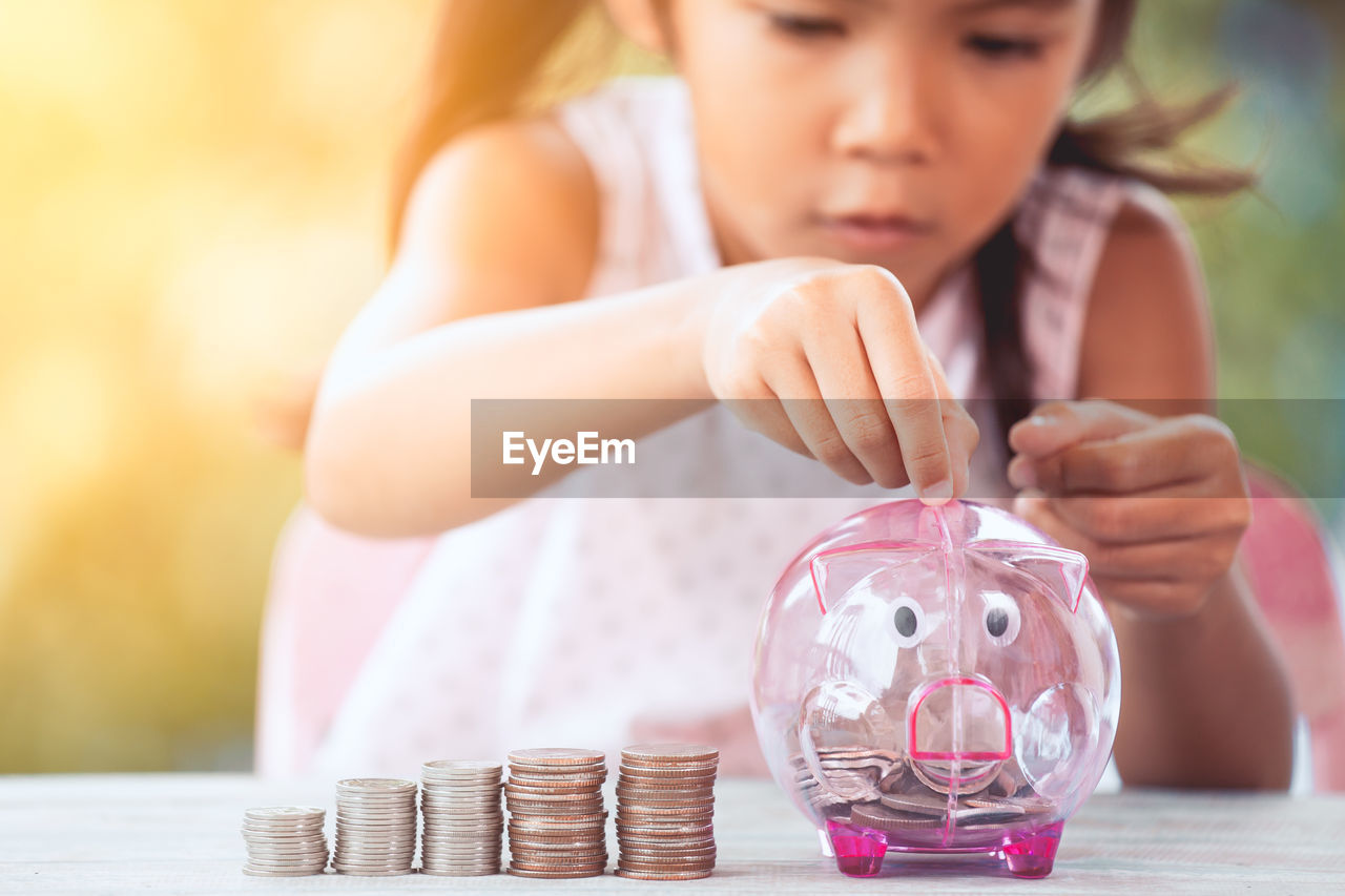 Girl putting coin in piggy bank at table