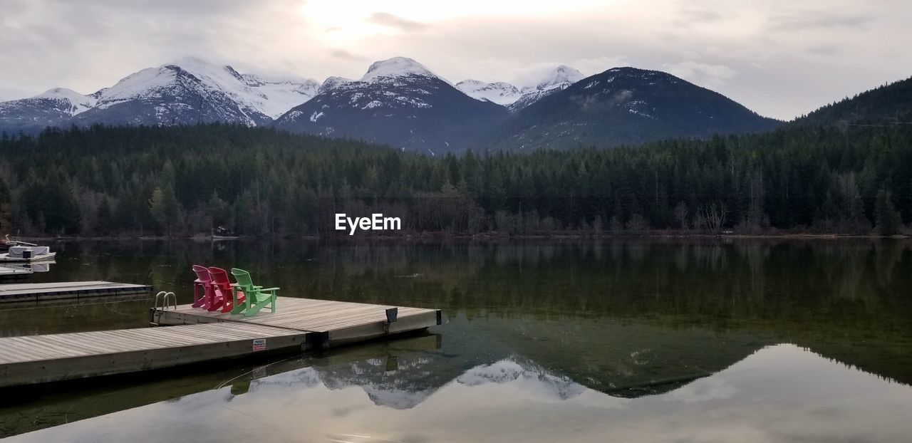 Colorful chairs on a dock with a view of the mountains from the shore of green lake in whistler, bc