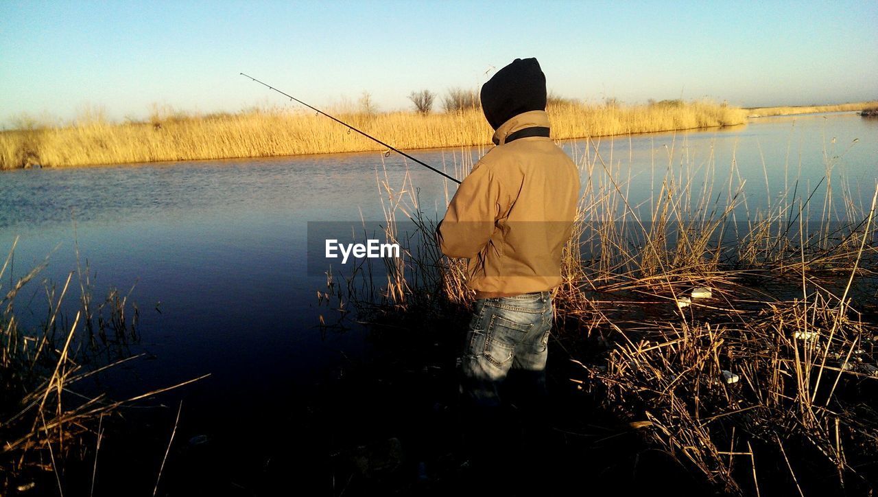 Rear view of man fishing at riverbank