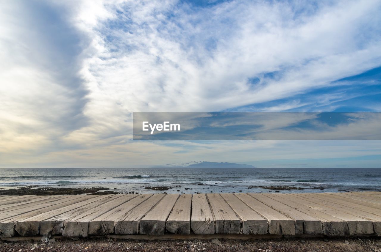 Boardwalk against the distant gomera island from the shore at playa de las americas in tenerife