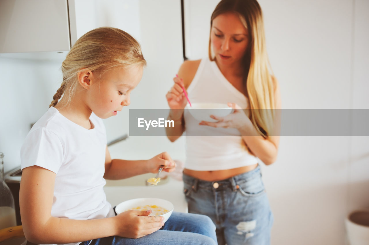 Mother with daughter eating food in kitchen at home