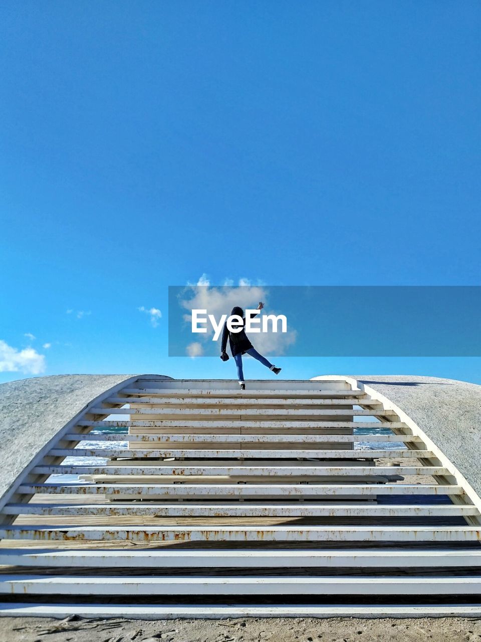 MAN JUMPING ON STEPS AGAINST BLUE SKY