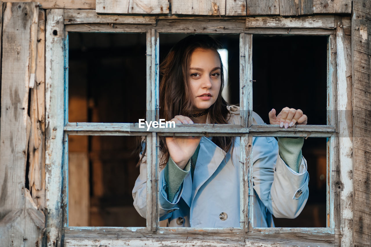 Girl looks out the window from an old wooden house