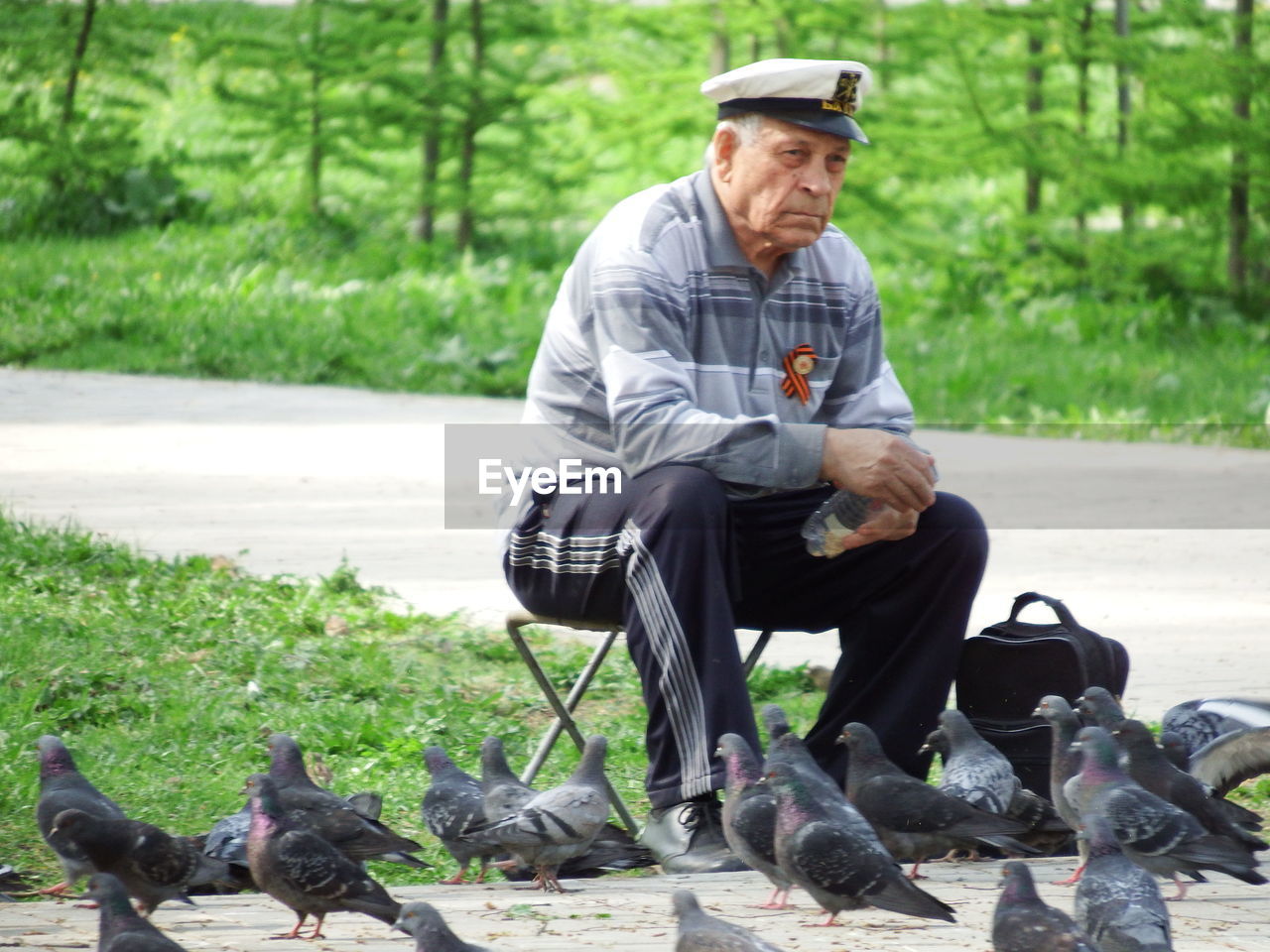 Senior man sitting on foldable chair while feeding pigeons at park