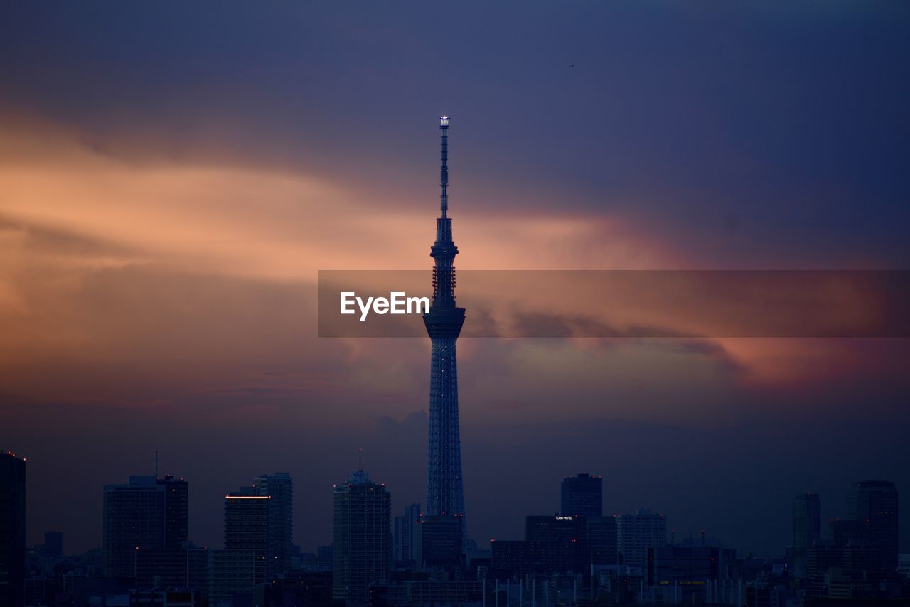 Communications tower in city against romantic sky at sunset