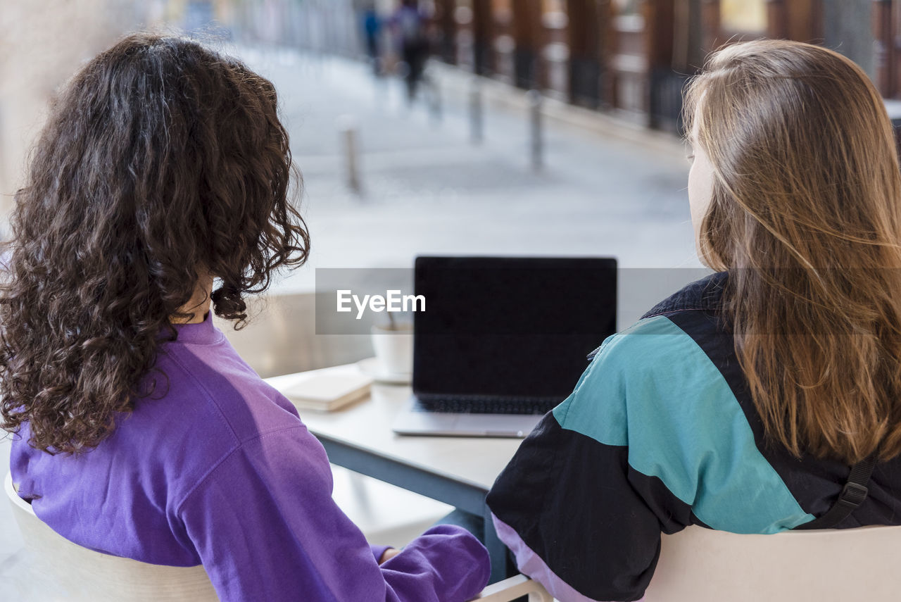 Two people using laptop and mobile phone while sitting outdoors at a coffee shop