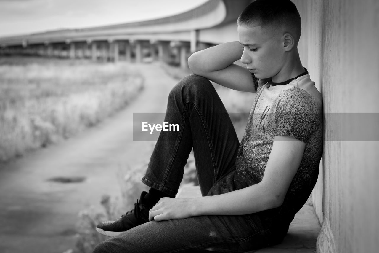 Side view of young man sitting against wall