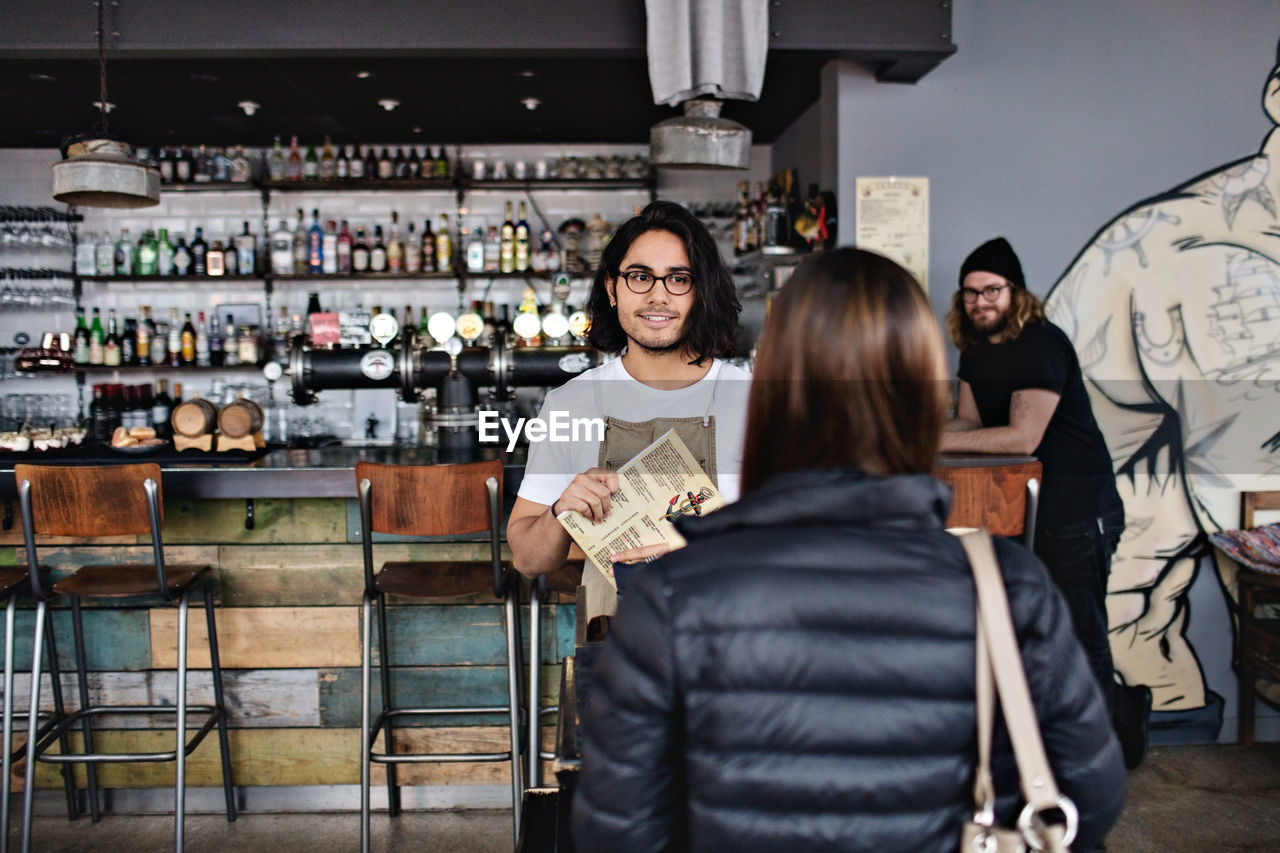 Waiter showing menu to female customer while standing at restaurant