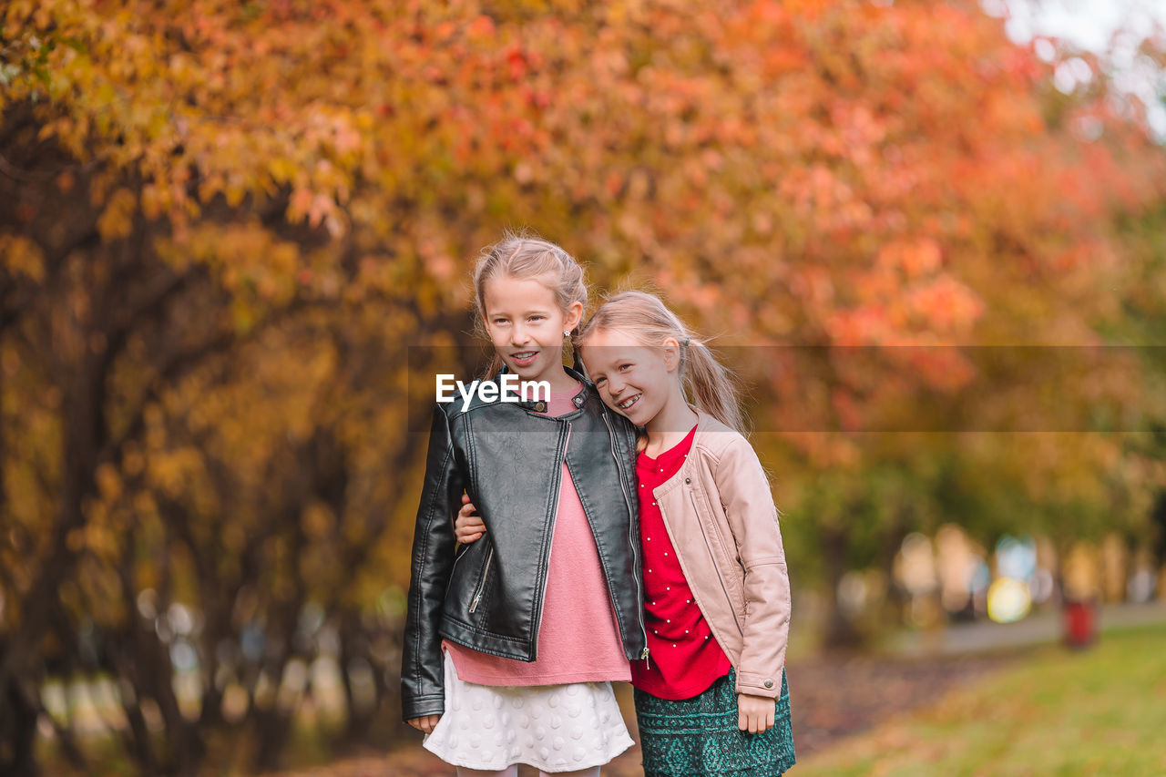 Cute smiling girls embracing while standing against autumn trees