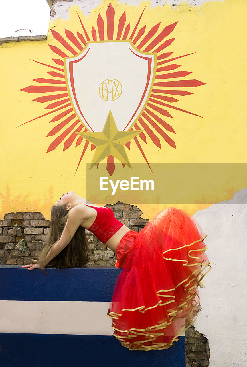 Side view of ballet dancer sitting on retaining wall