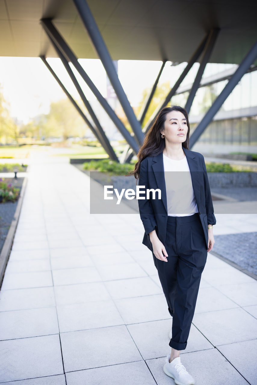 Full body portrait of asian confident business woman in suit, walking in business center spring park