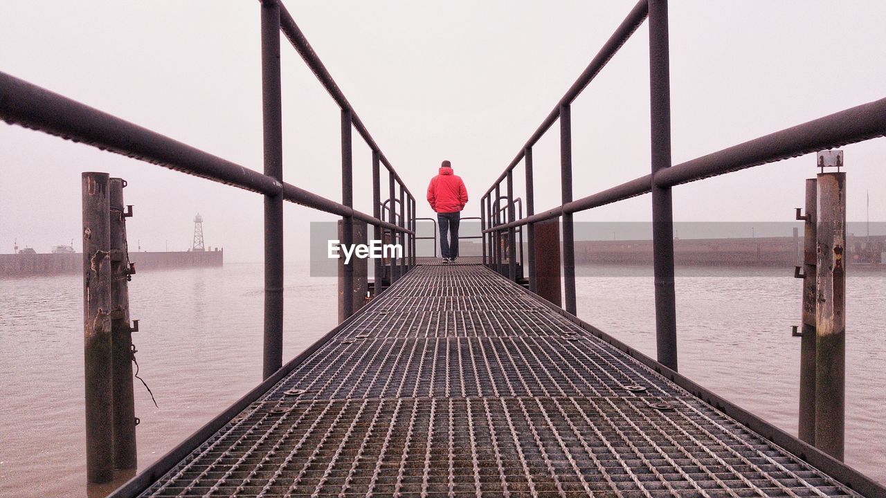 Rear view of man standing on pier by sea against sky