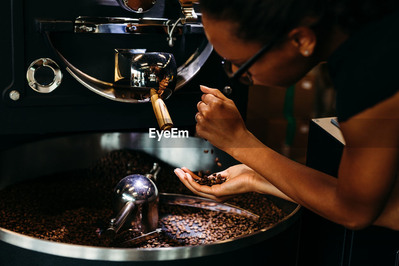 Close-up of woman with roasted coffee beans in machinery at cafe