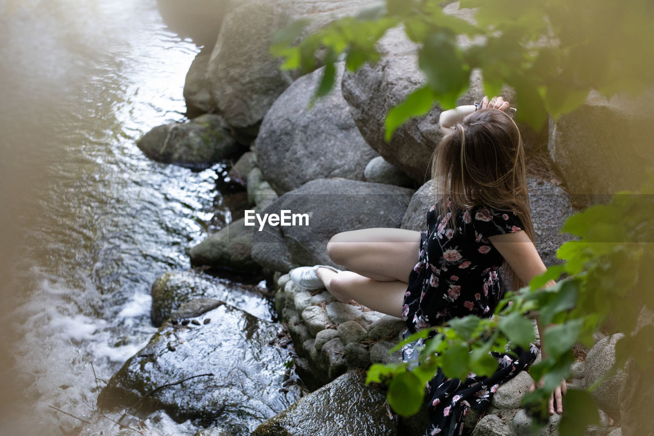 HIGH ANGLE VIEW OF WOMAN SITTING ON ROCKS