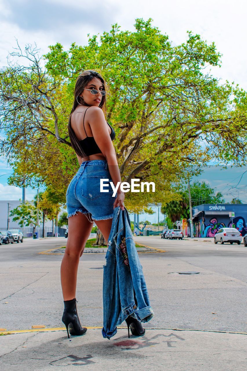 Full length portrait of young woman standing on road