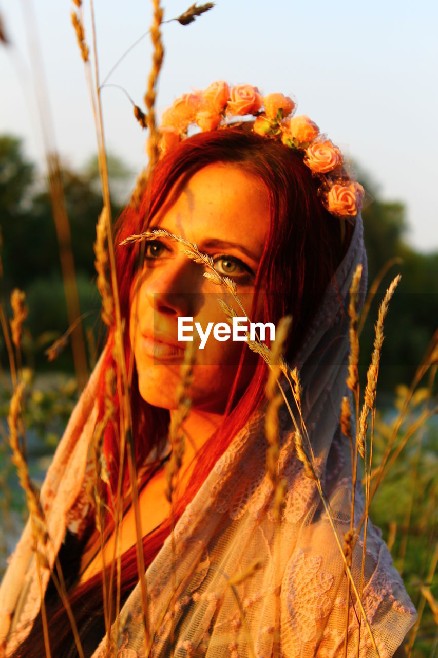 Close-up of thoughtful woman by wheat crop during sunset