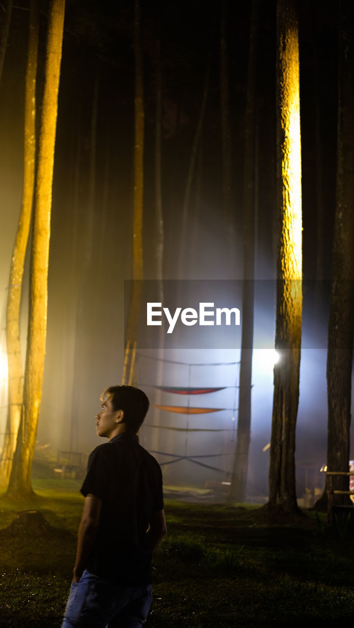 REAR VIEW OF WOMAN LOOKING AT ILLUMINATED CAMERA