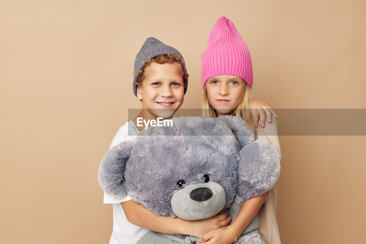 Portrait of sibling holding stuffed toy against beige background