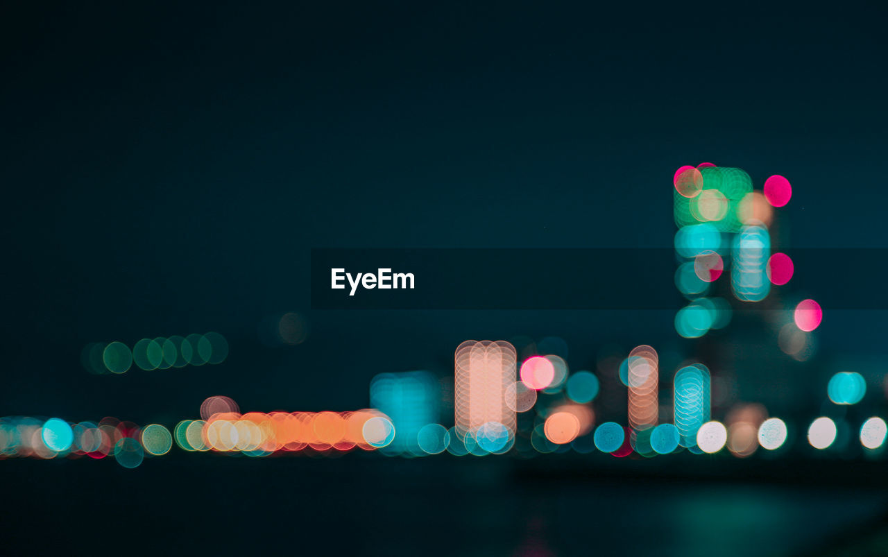 Defocused image of illuminated lights in city against sky at night