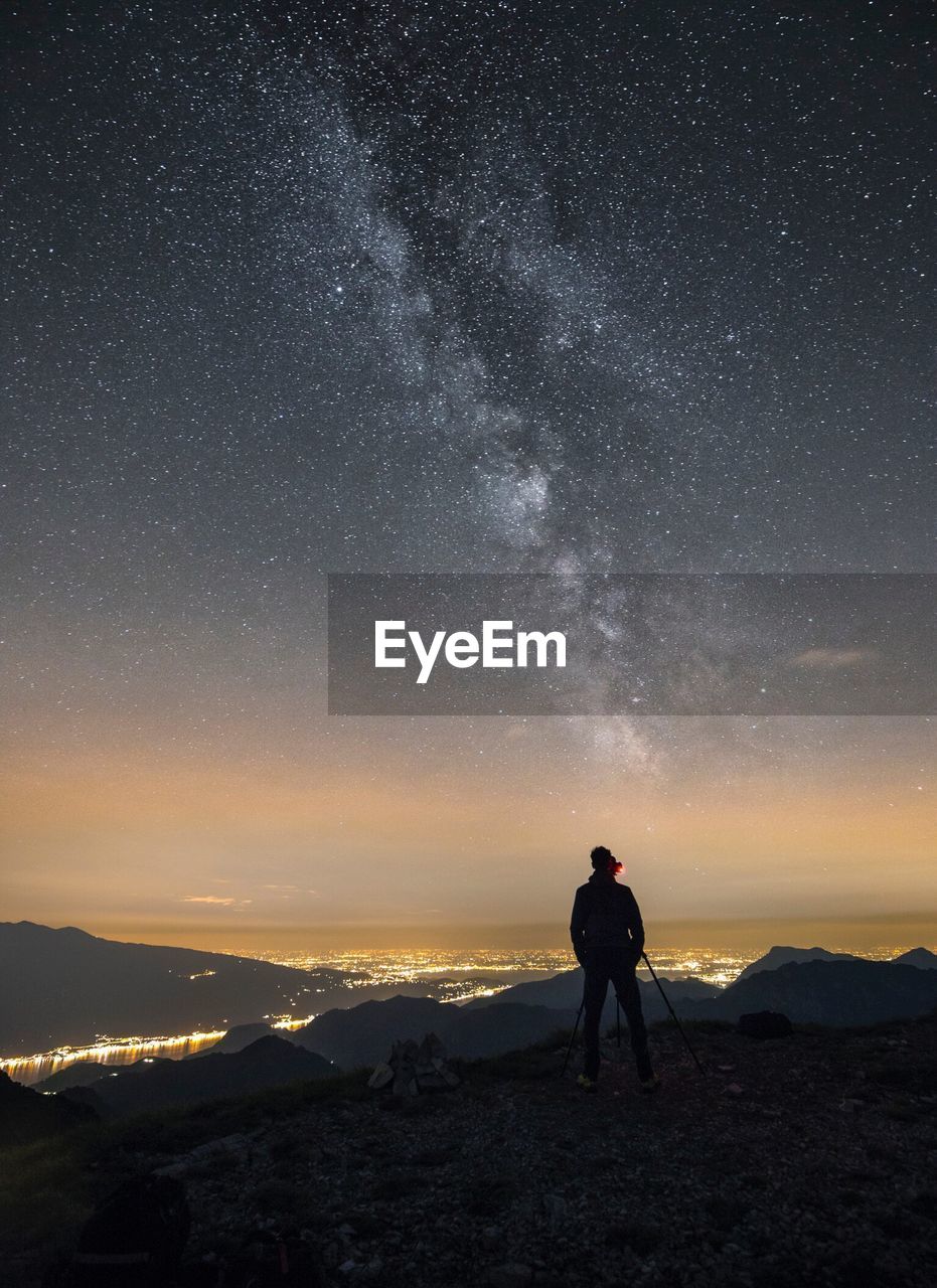 Rear view of silhouette man photographing on mountain against star field at night