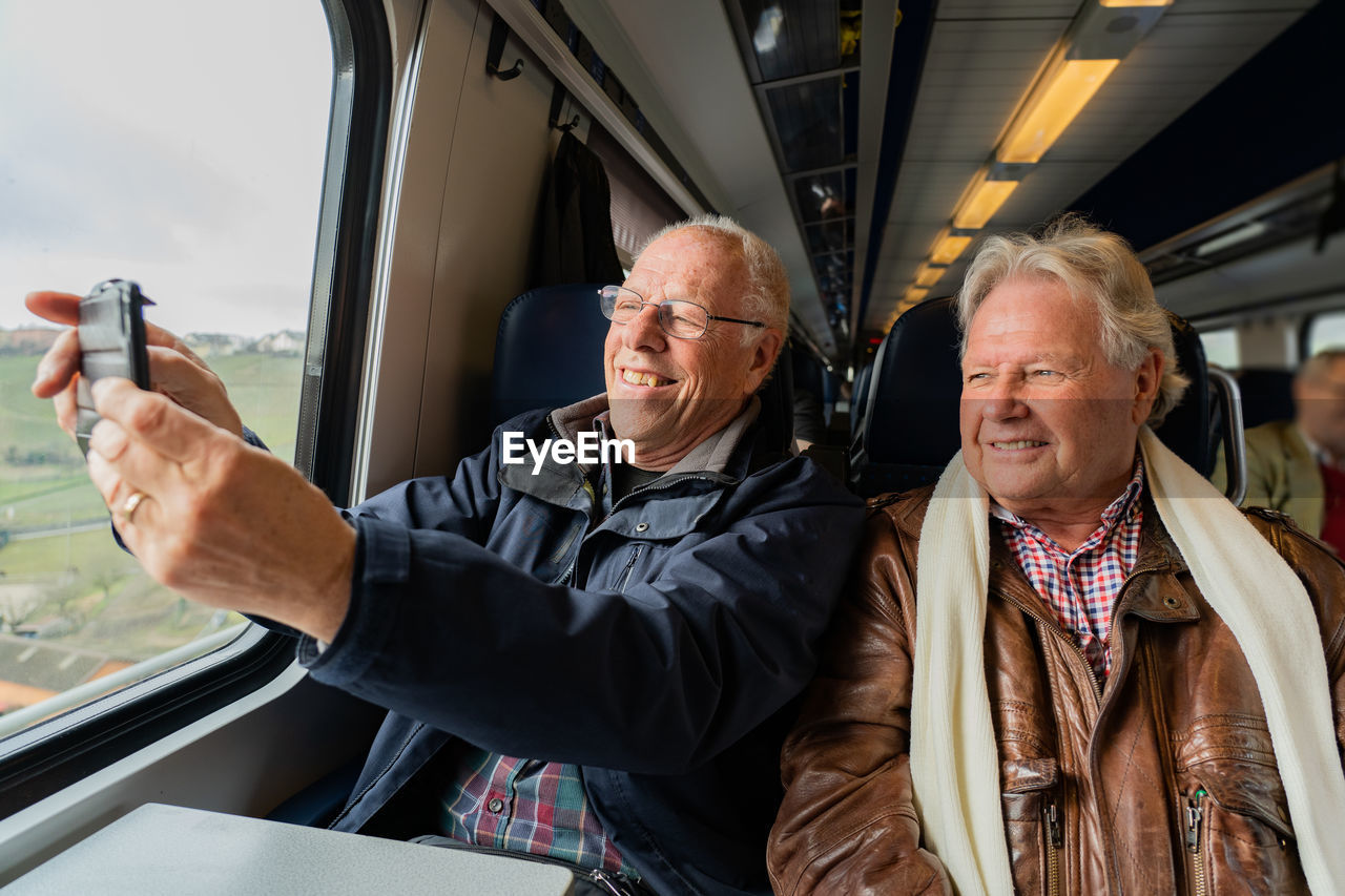 Smiling senior friends taking selfie while sitting in train