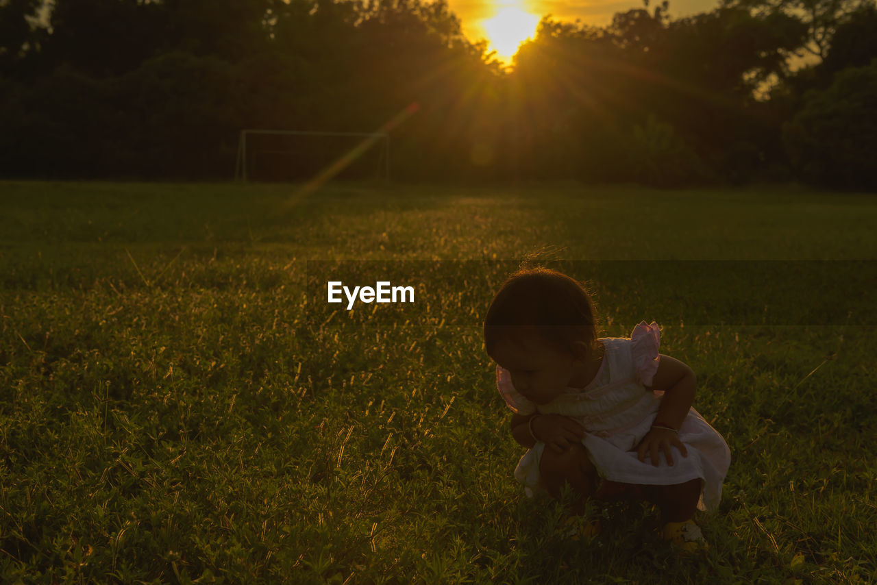 Rear view of girl on field against sky during sunset