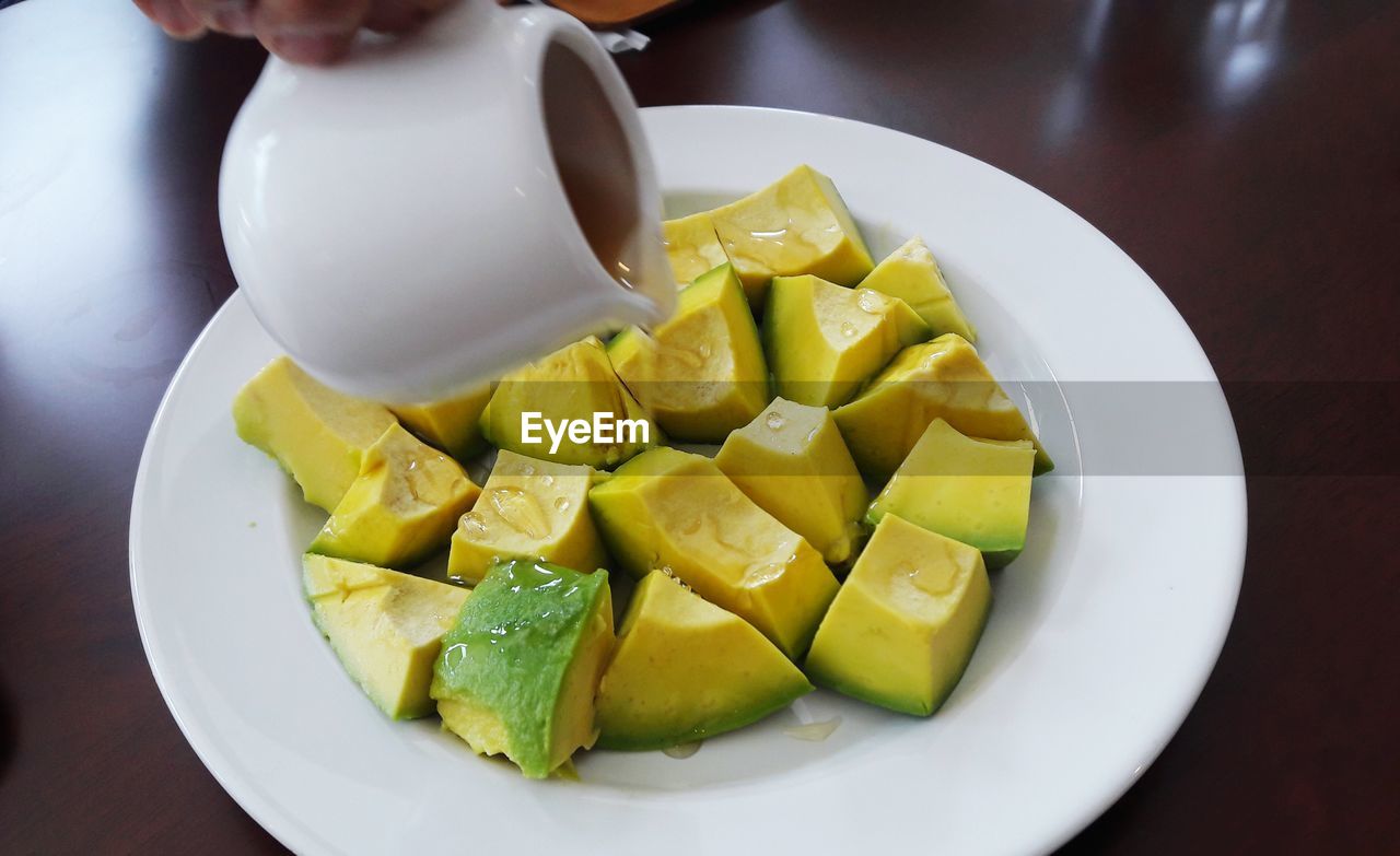 Close-up of jug pouring syrup on chopped avocados in plate at table