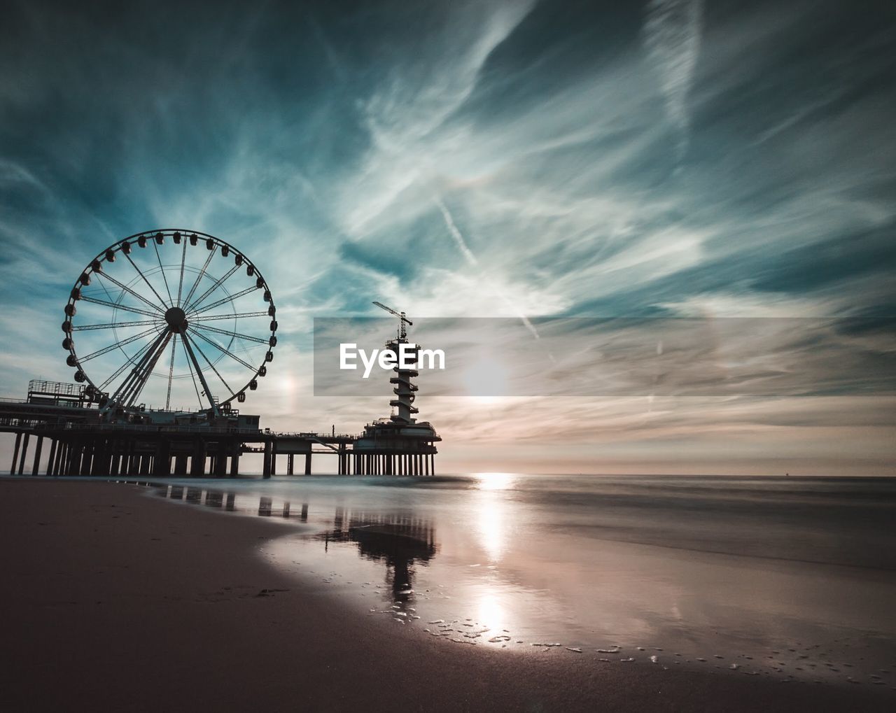 Silhouette ferris wheel at beach during sunset