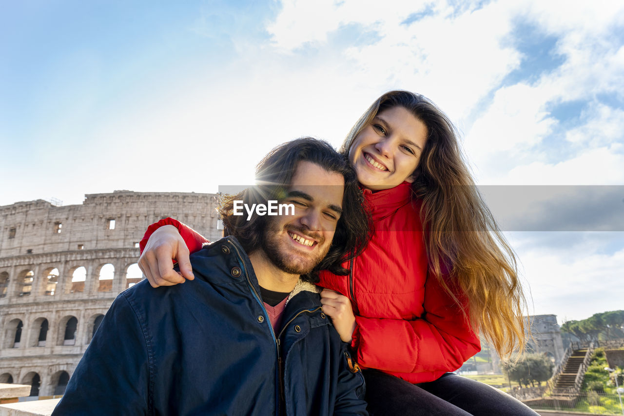 Young couple traveling to rome. the couple smiles and takes a selfie in front of the colosseum.