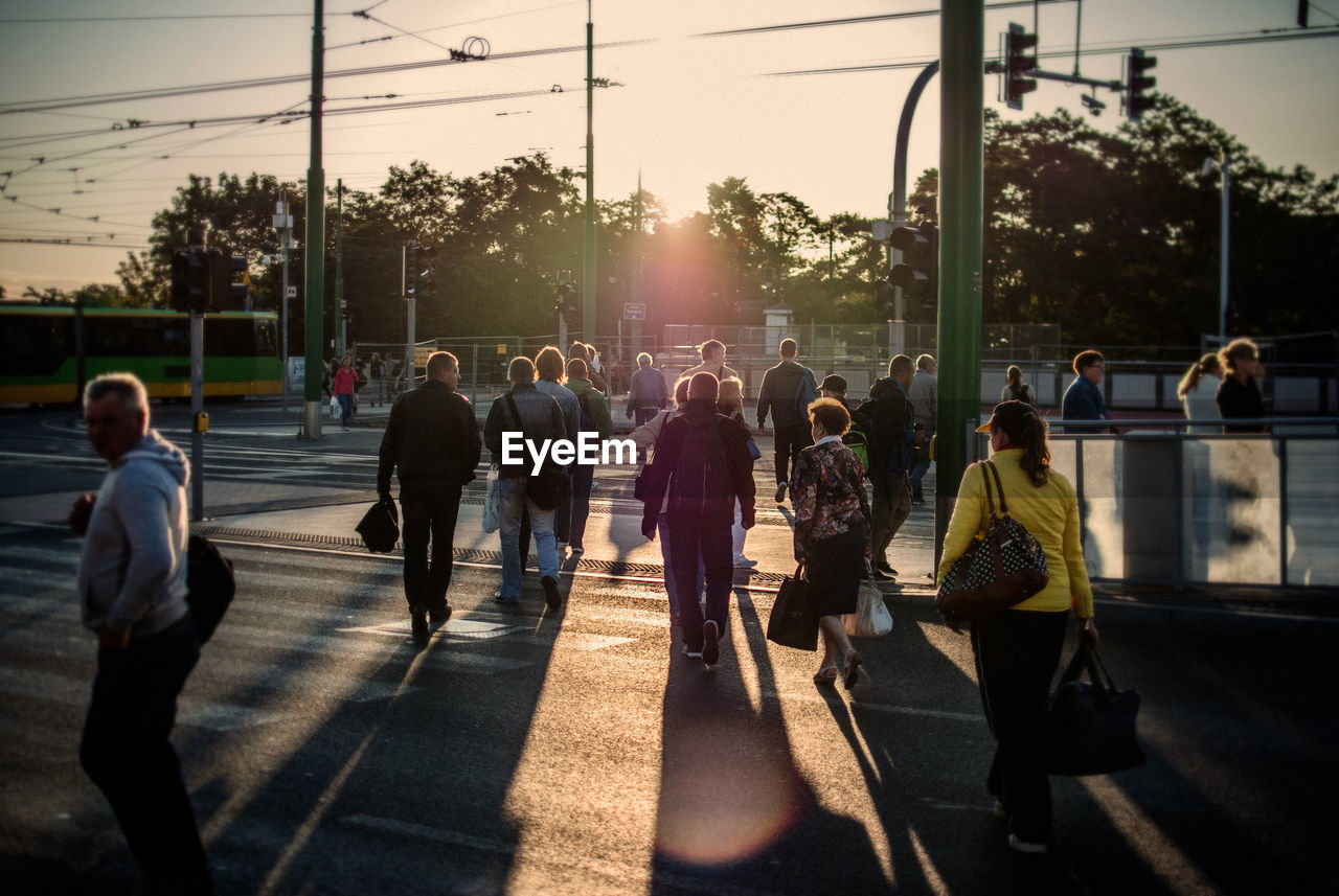 Rear view of people crossing street in city during sunset