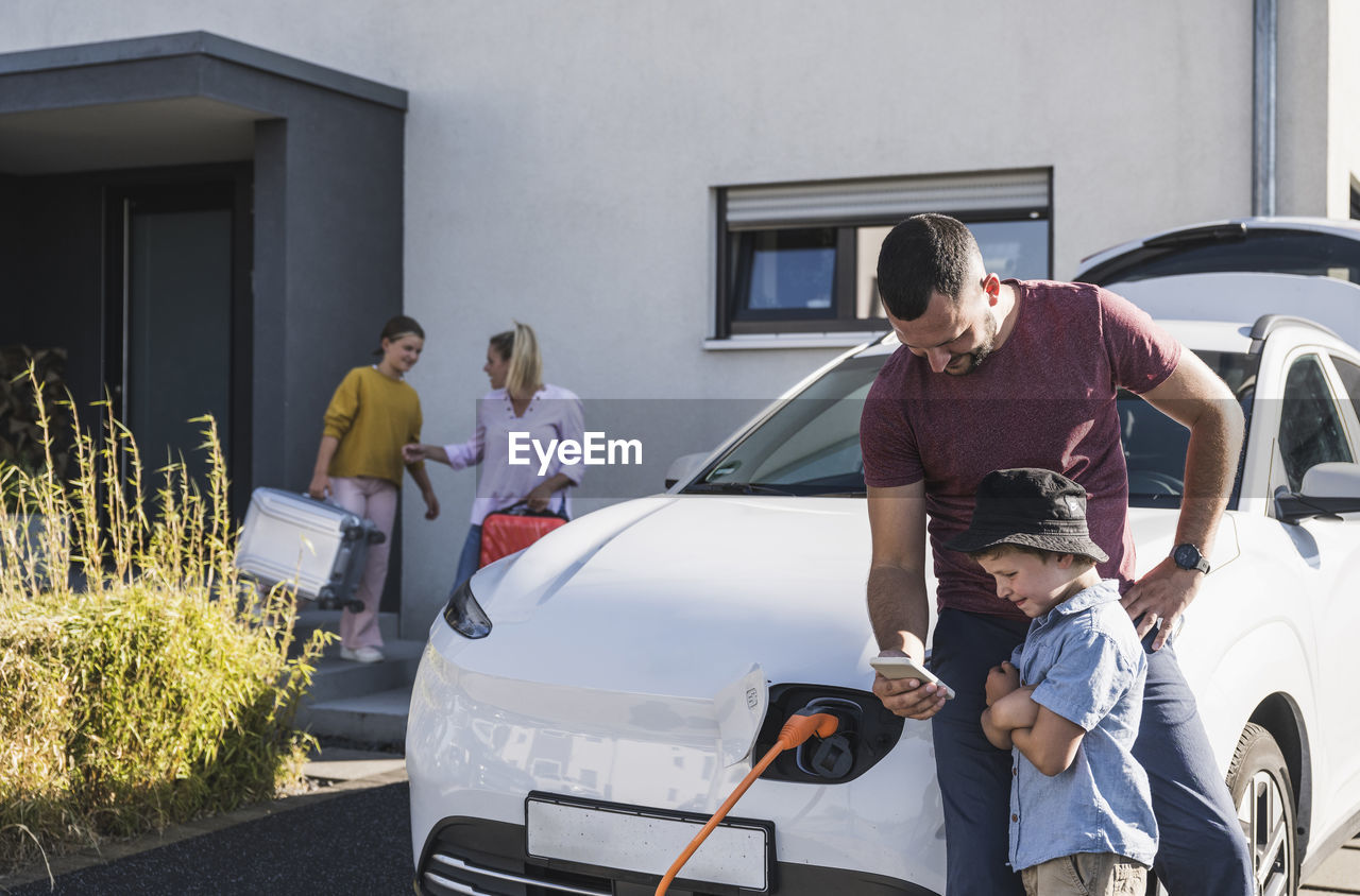 Father and son checking smartphone by charging electric car