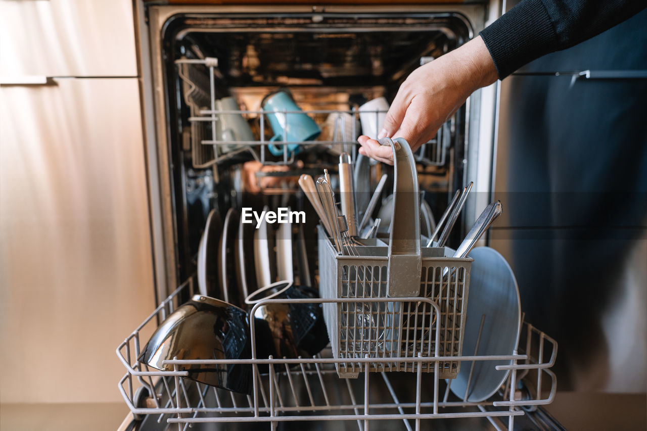 Midsection of man loading dishwasher machine in kitchen at home