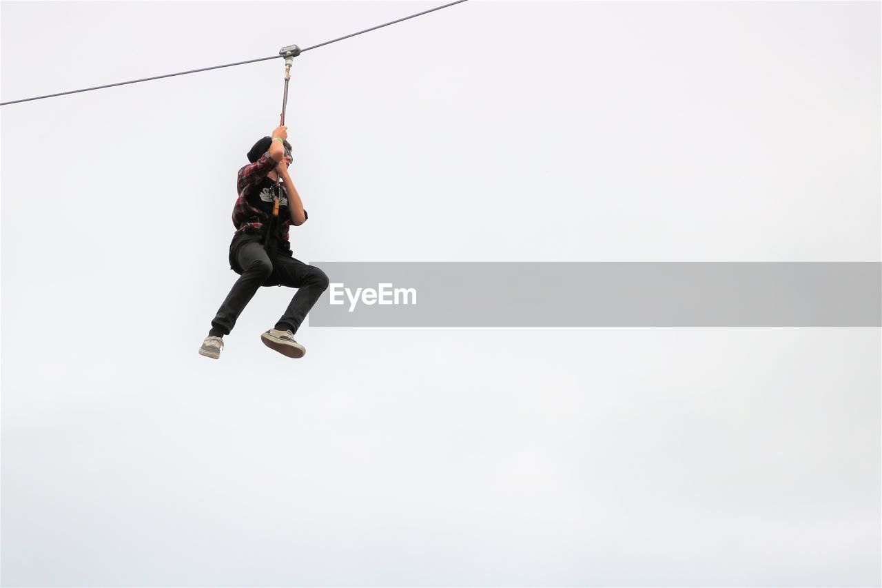 Low angle view of teenage boy zip lining against sky