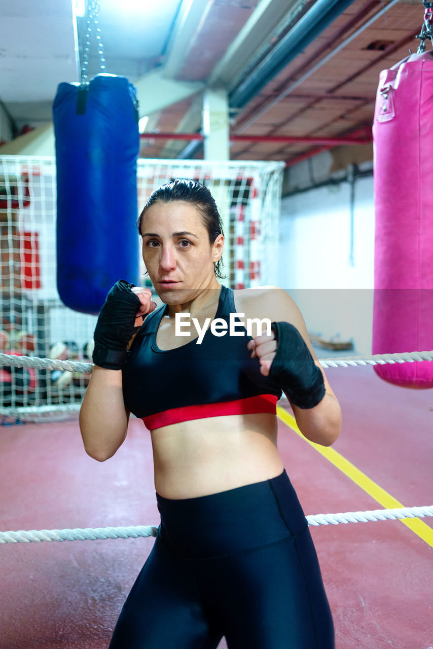 Real female boxer in gloves leaning on rope at ring before training