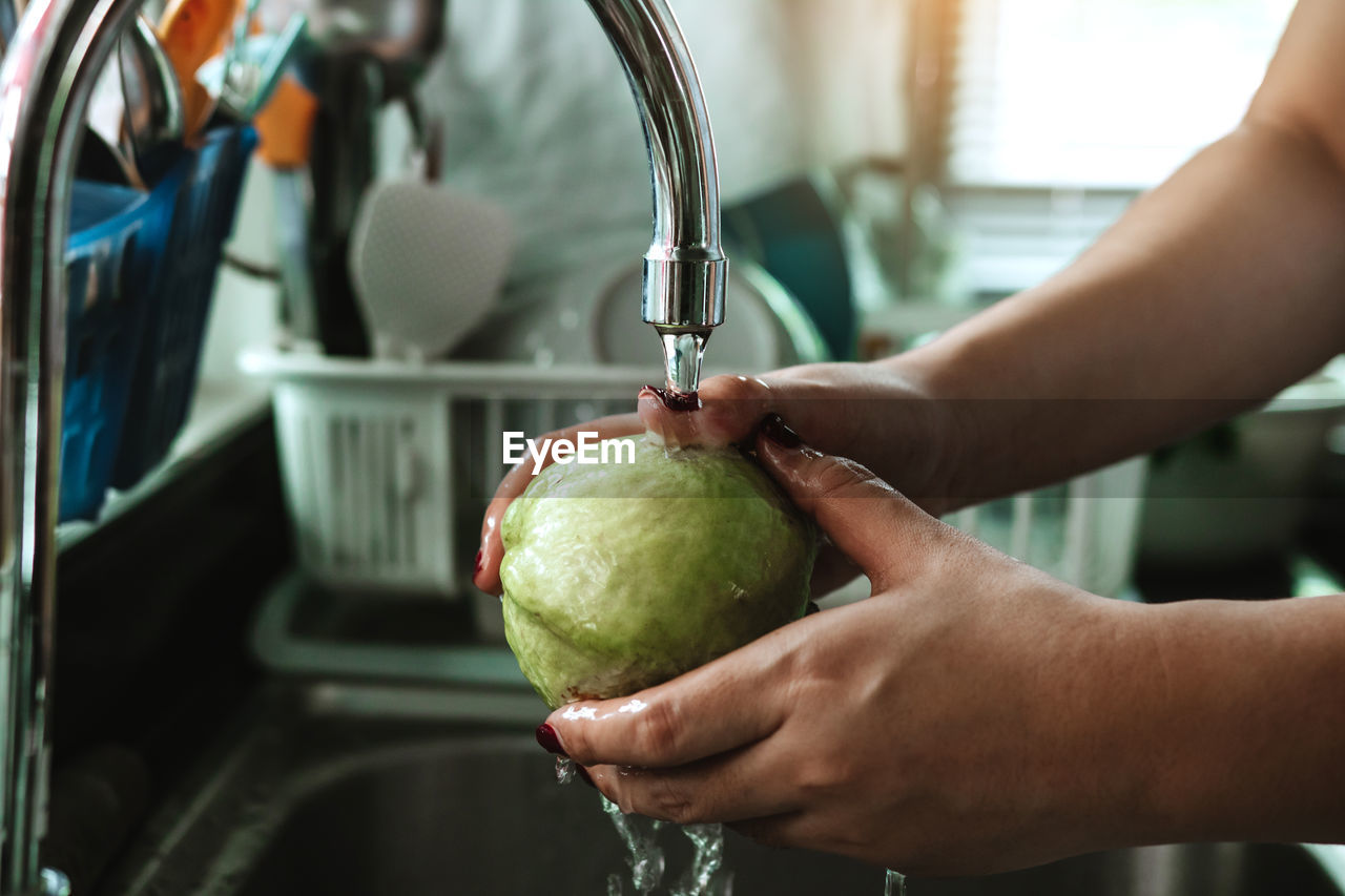 Cropped hand of woman cleaning fruit at sink