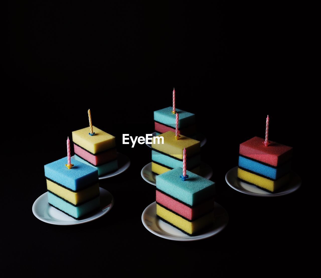 Close-up of candles over multi colored sponge stacked in plate against black background