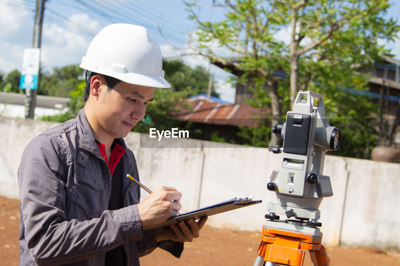 Engineer writing on paper by theodolite at construction site