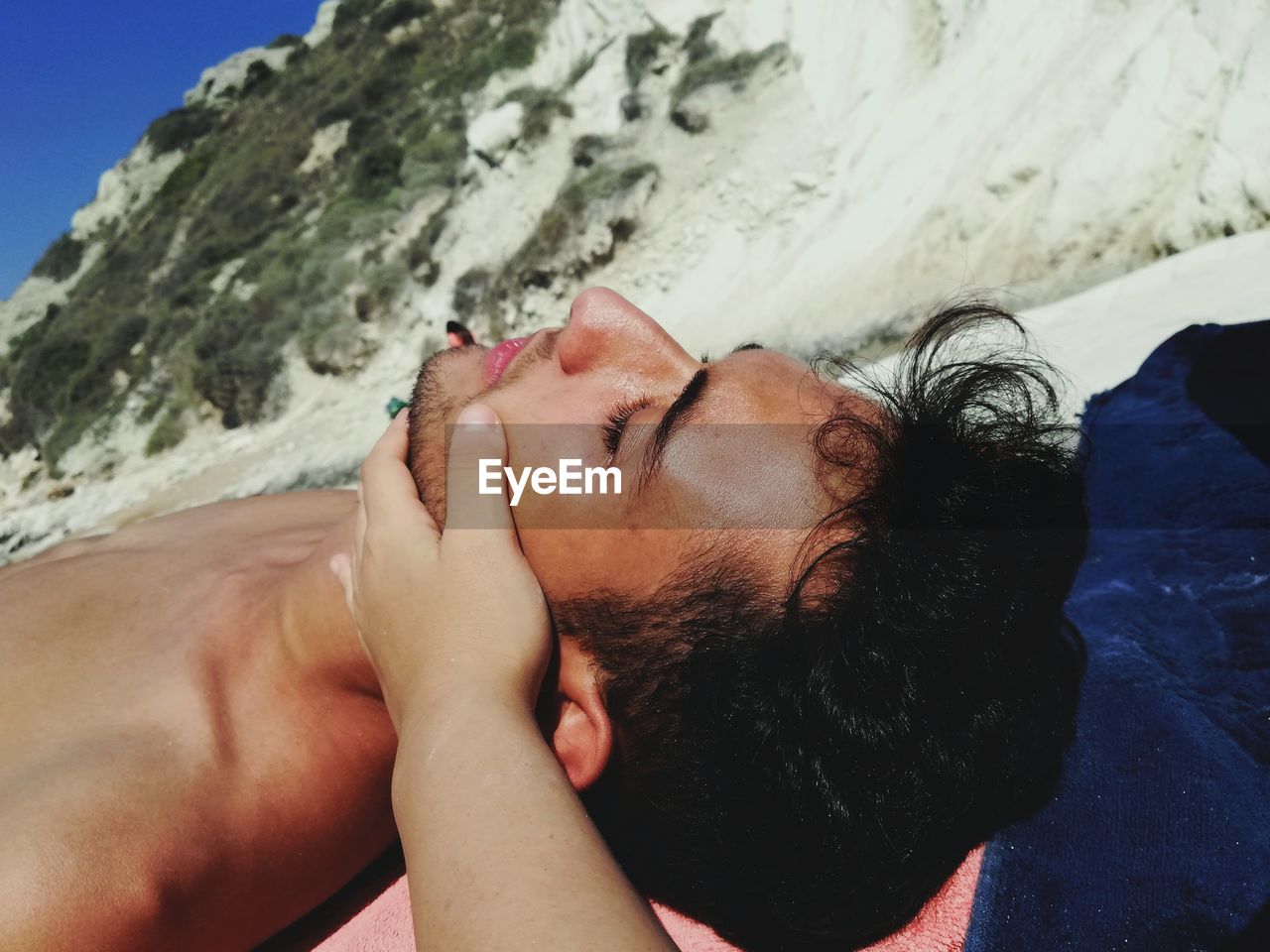 Hand touching face of man while relaxing at shore of beach