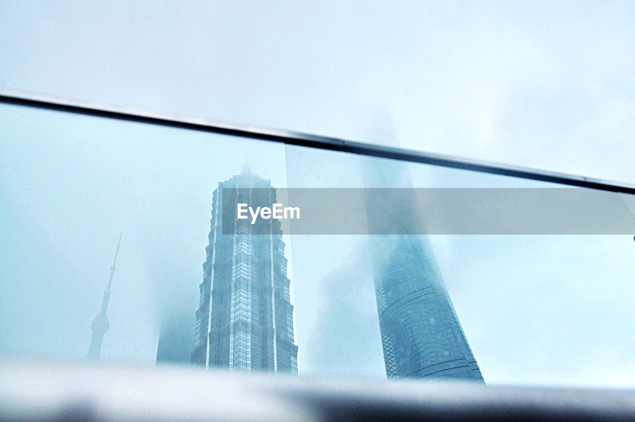 Low angle view of skyscrapers against sky during foggy weather