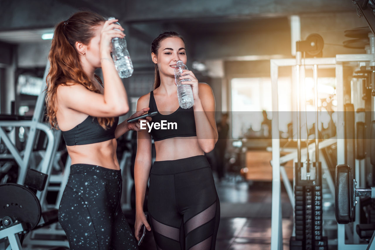 Women drinking water while standing in gym