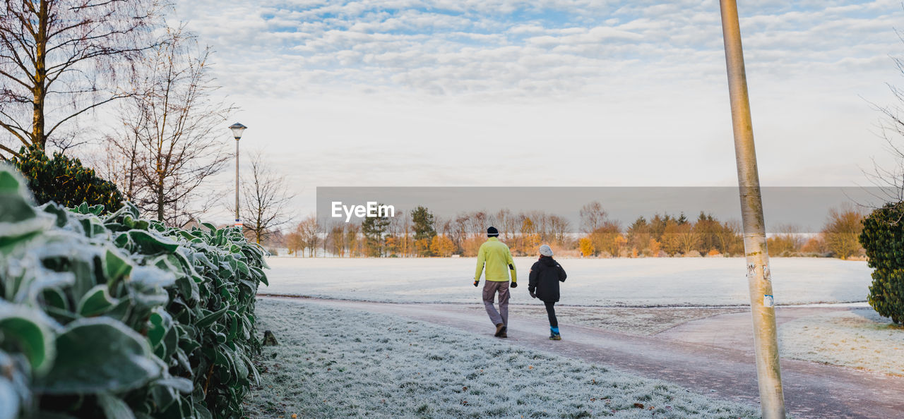 Rear view of people walking on snowy field against sky