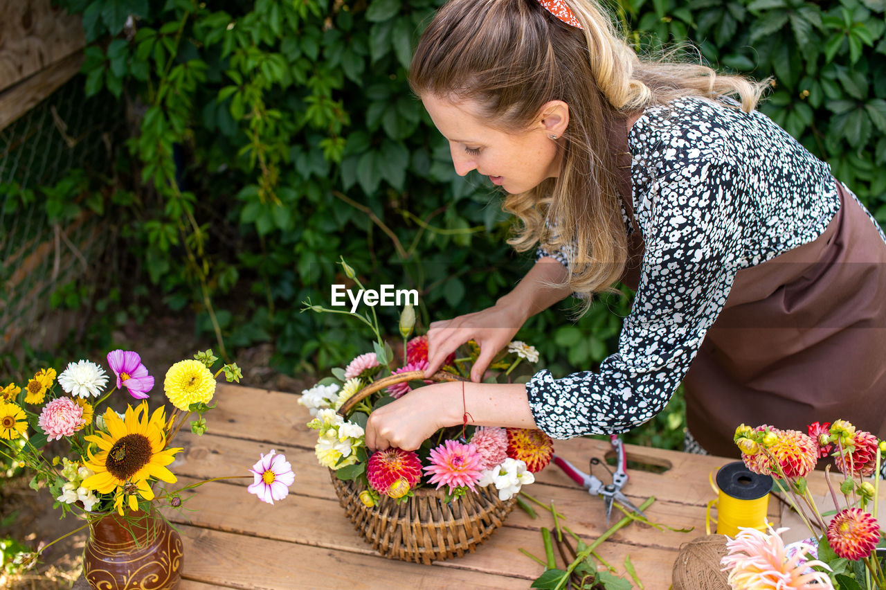 Cute florist girl collects a bouquet of autumn flowers in a basket on the table