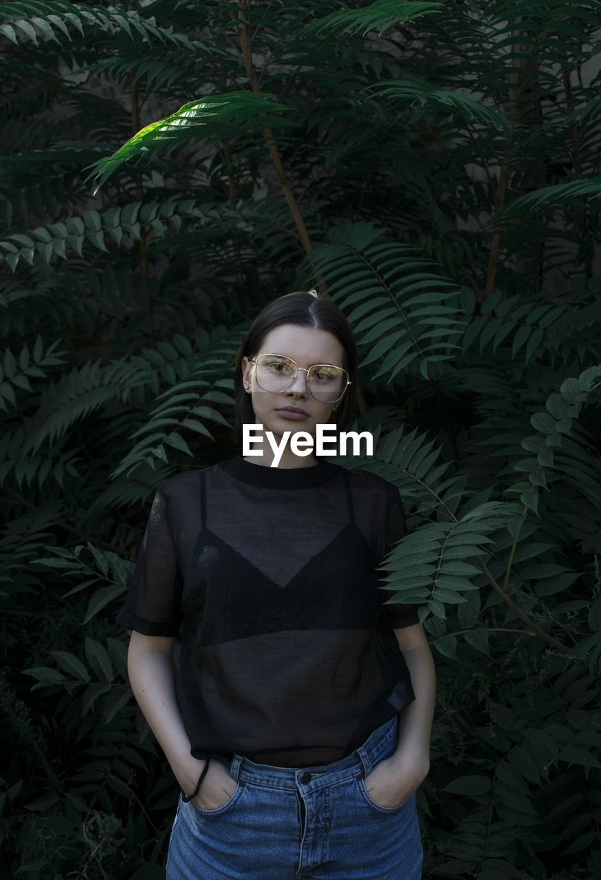 Portrait of young woman standing against plants