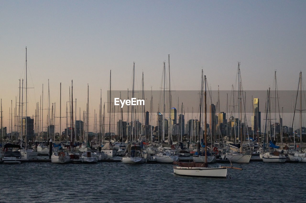 Sailboats moored in sea against clear sky during sunset