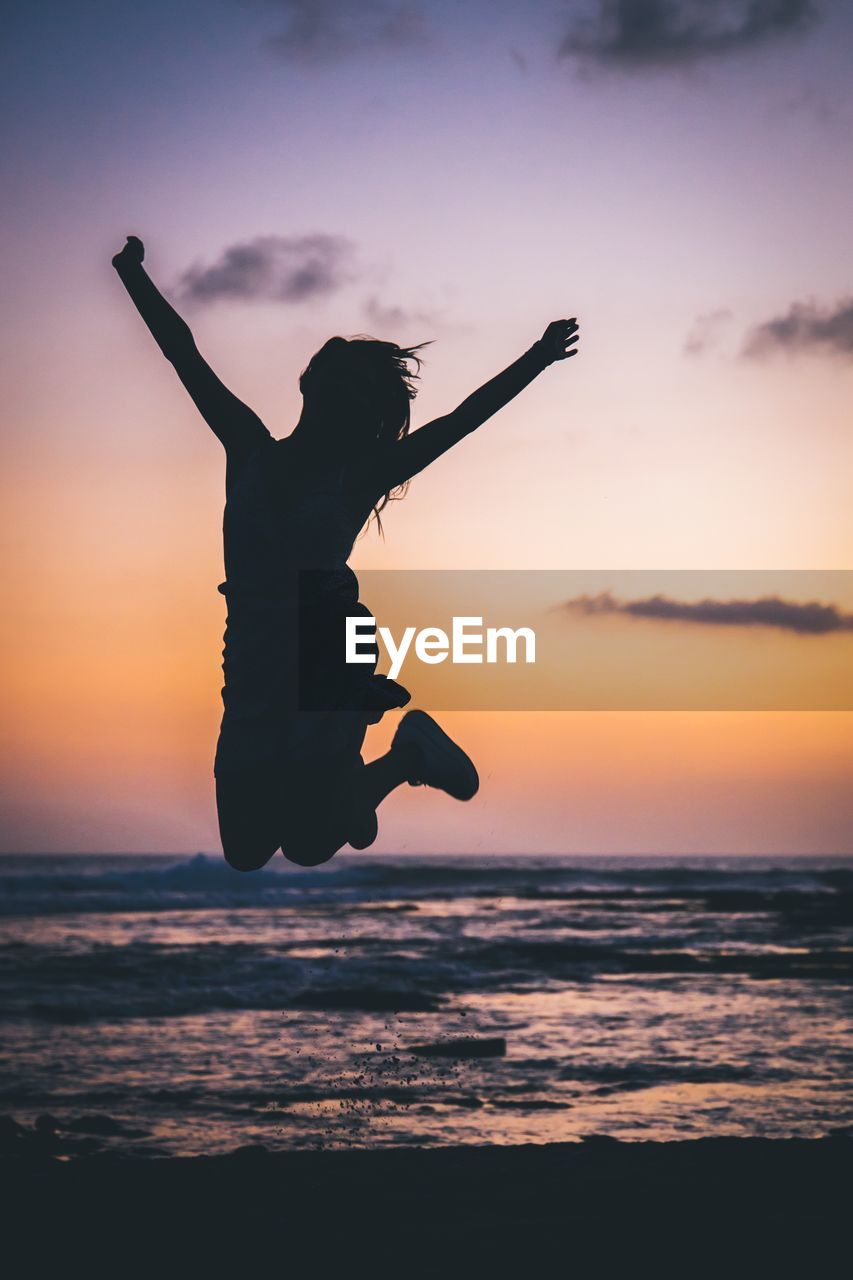 Silhouette woman jumping on beach against sky during sunset