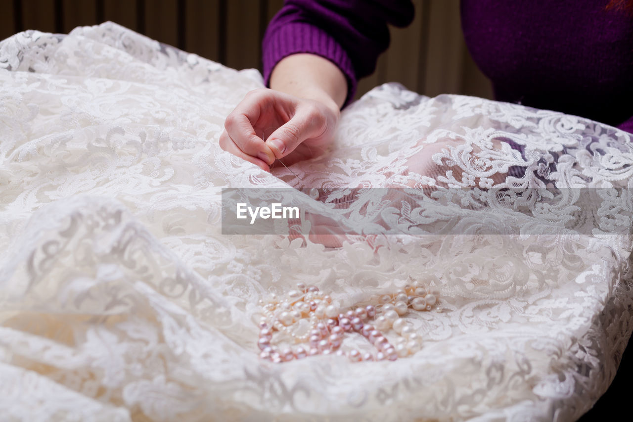 Cropped hand of woman stitching pearls on white wedding dress