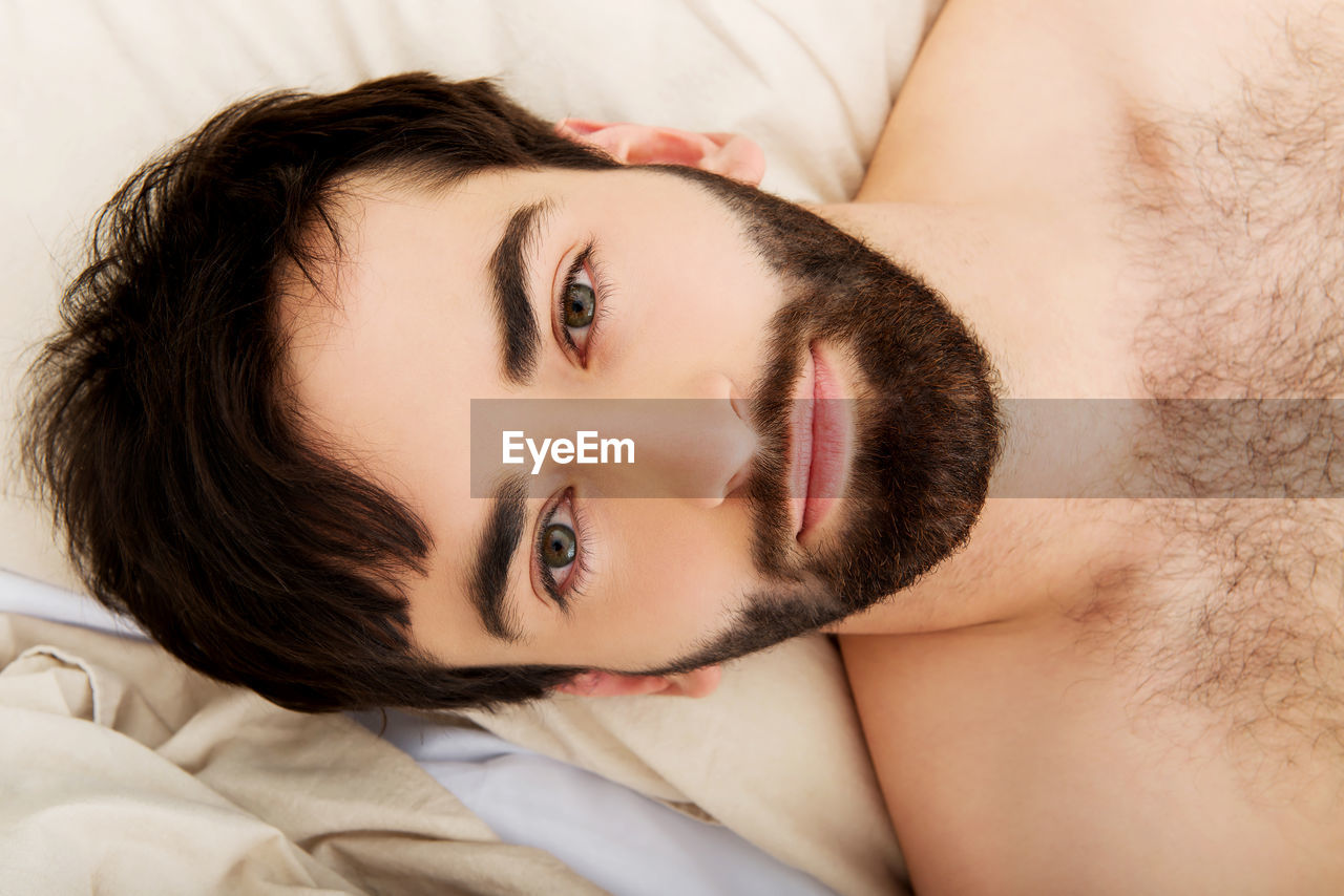 Portrait of shirtless young man relaxing on bed